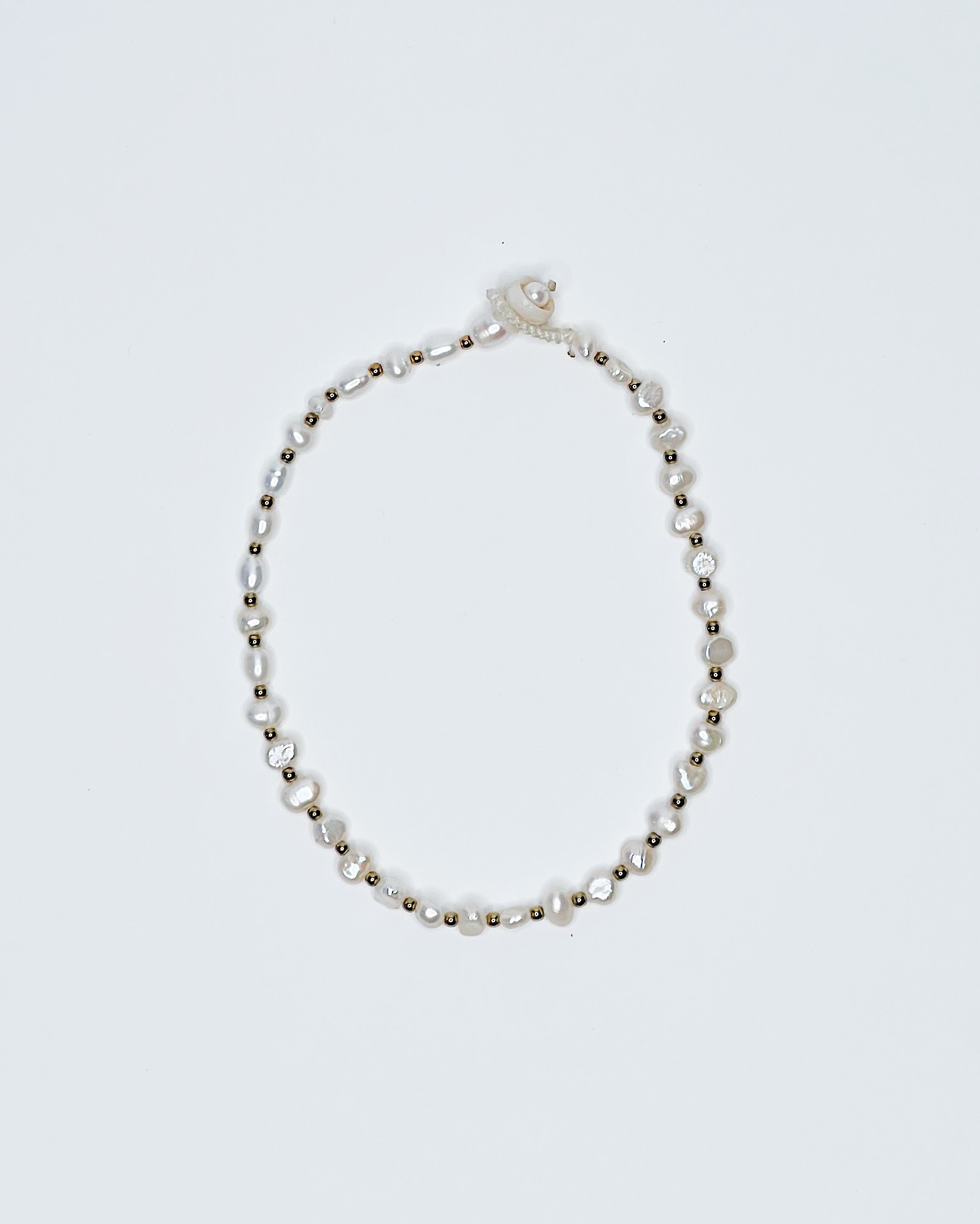 Handmade anklet featuring freshwater pearls and gold bead spacers, finished with a natural puka shell clasp, displayed against a clean white background