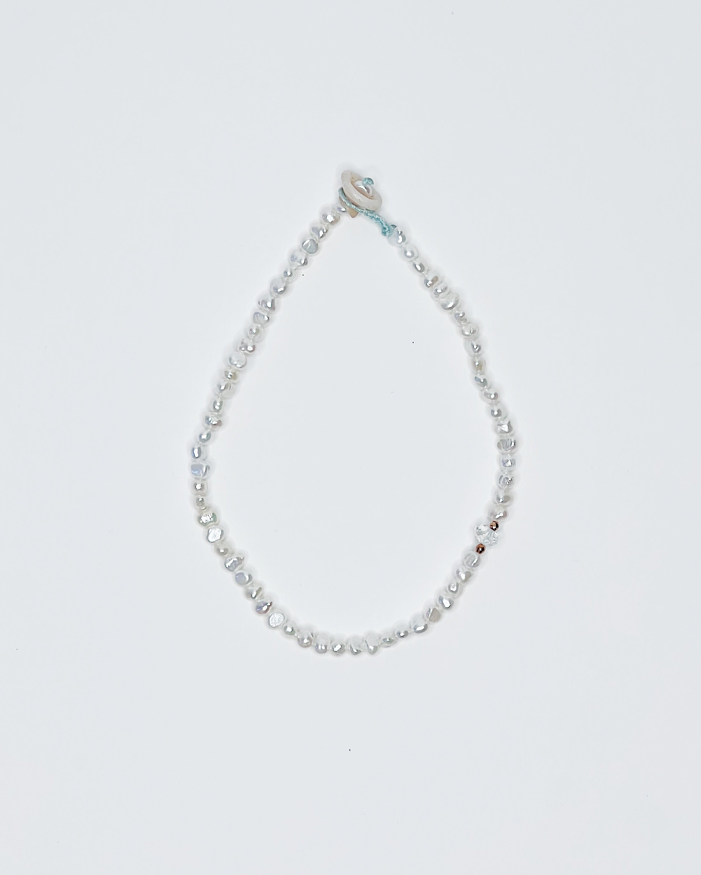 Handmade anklet featuring freshwater pearls, finished with a natural puka shell clasp, displayed against a clean white background