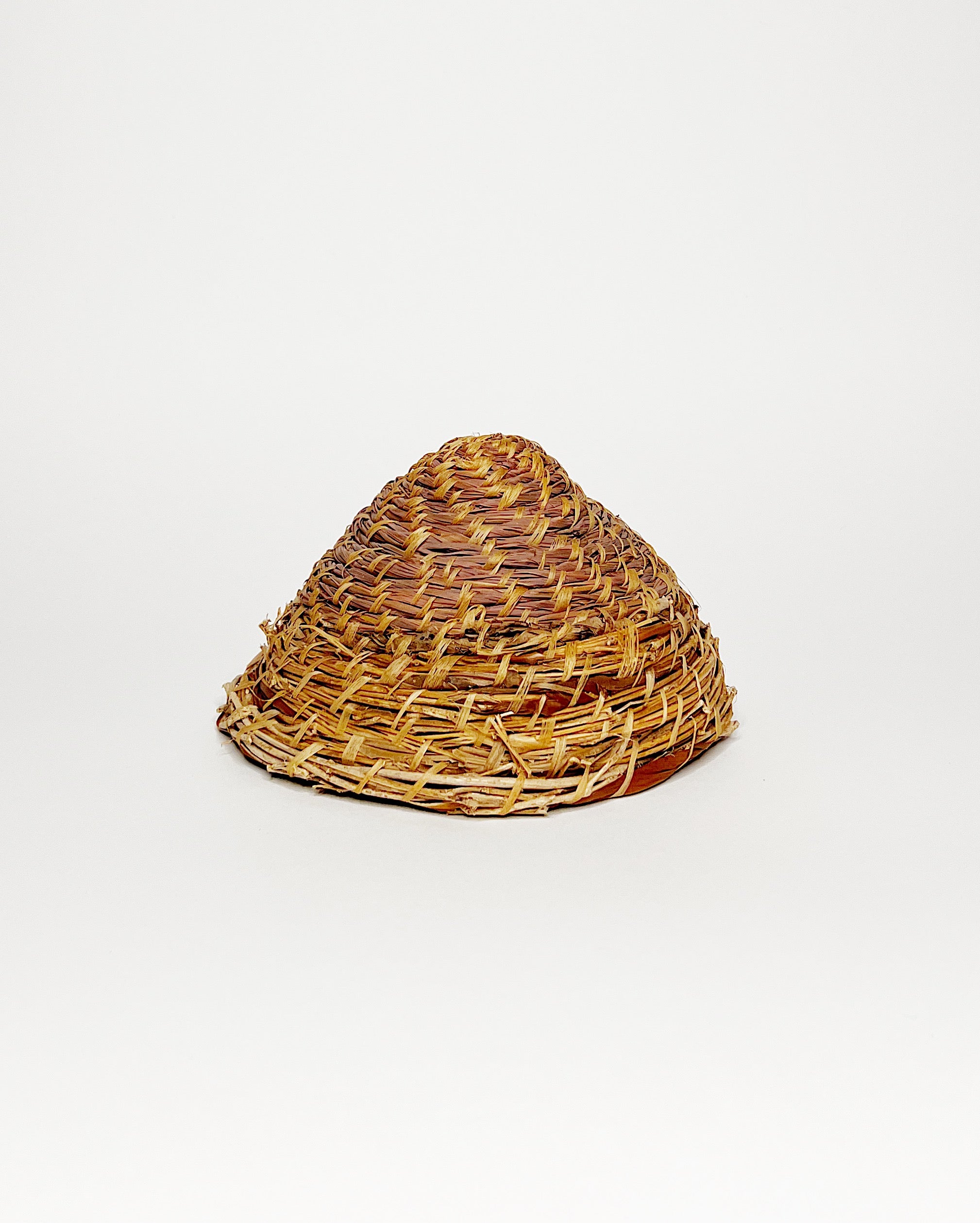Handwoven basket crafted from lemongrass, lauaʻe fern, morning glory vine, and hau fiber, featuring a natural spiral weave pattern and a small organic handle, displayed against a clean white background. Underside view.