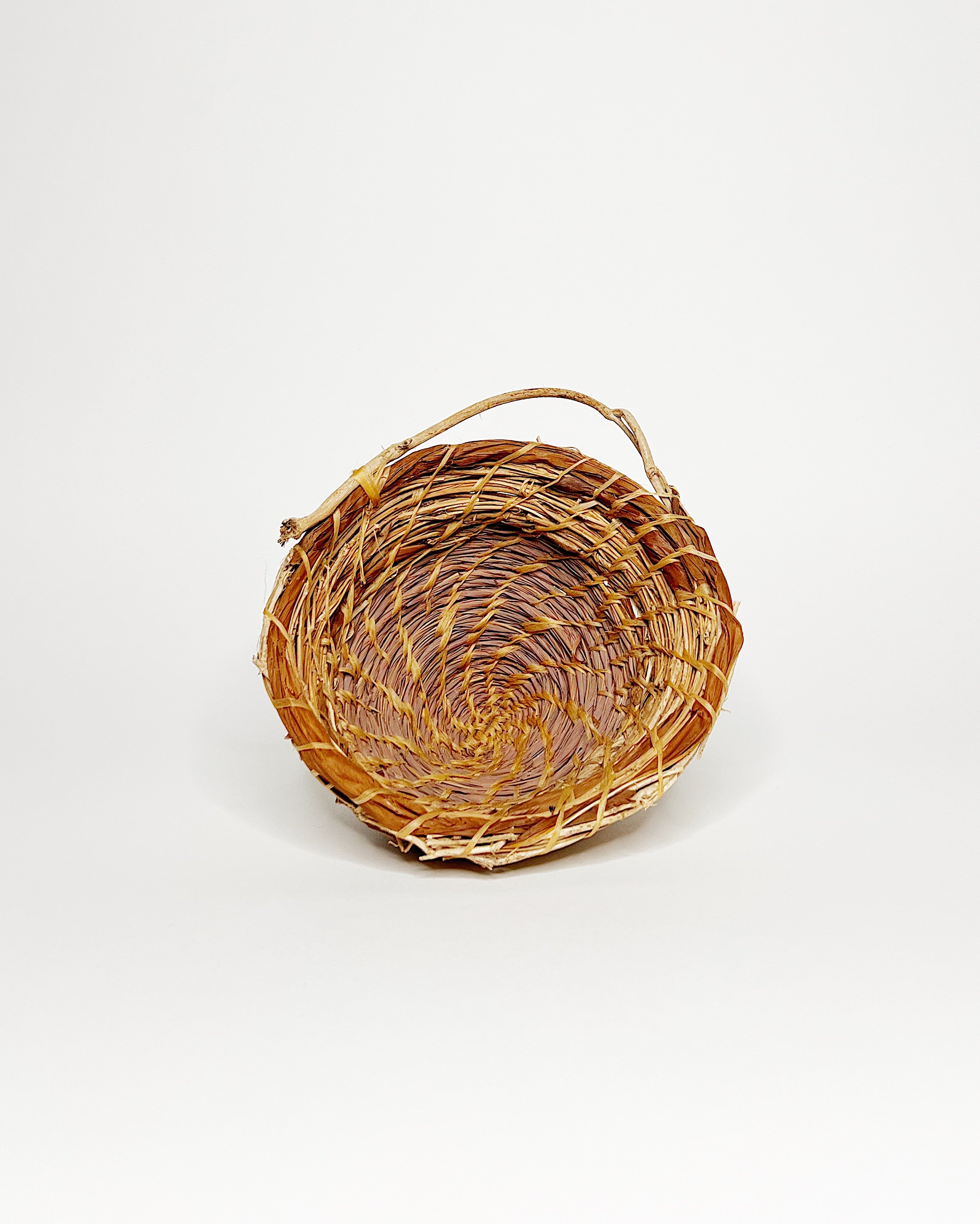 Handwoven basket crafted from lemongrass, lauaʻe fern, morning glory vine, and hau fiber, featuring a natural spiral weave pattern and a small organic handle, displayed against a clean white background