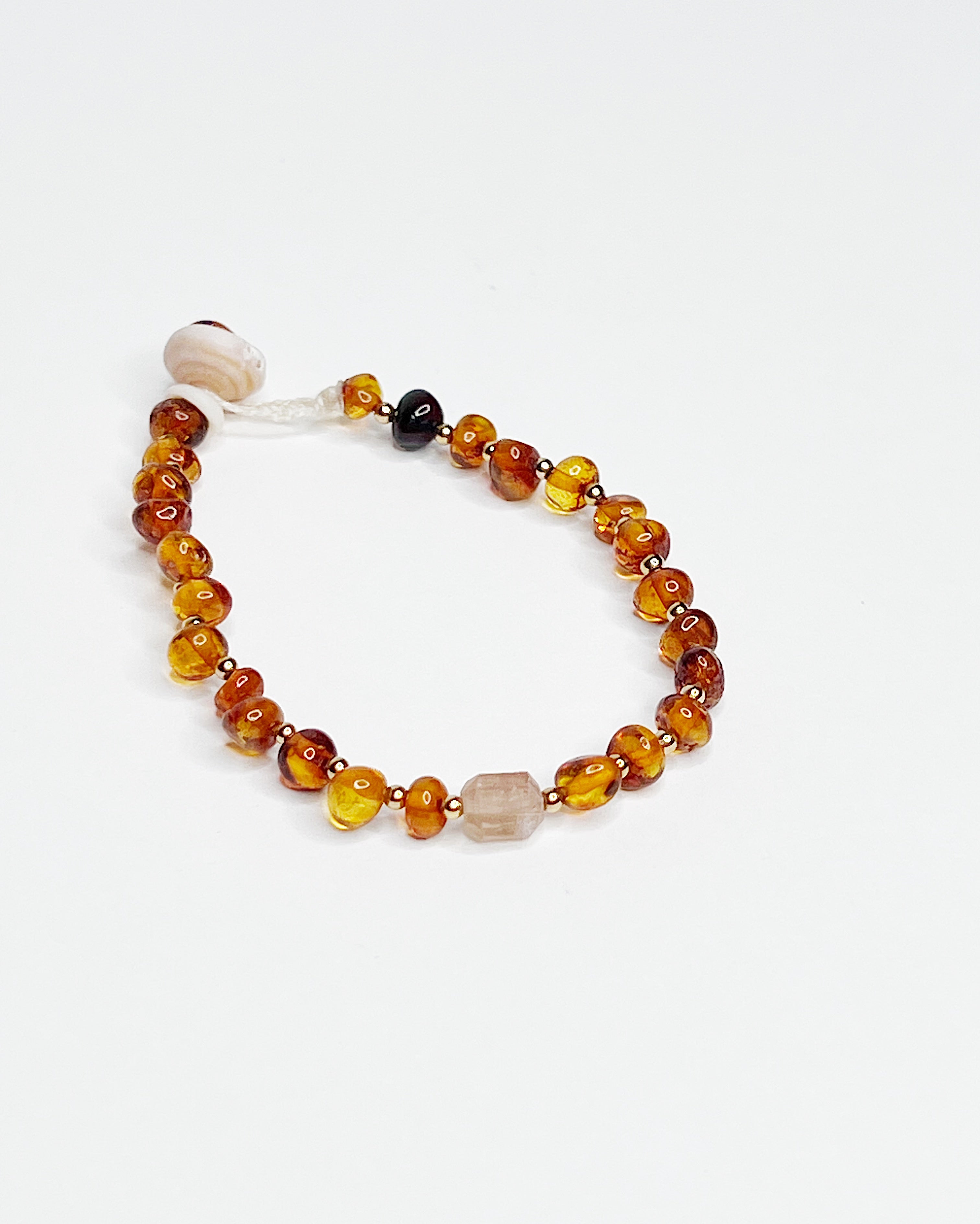Handmade bracelet featuring polished Baltic amber beads in cognac tones, accented with tiny gold spacers and finished with a tourmaline crystal and natural puka shell clasp, displayed on a white background