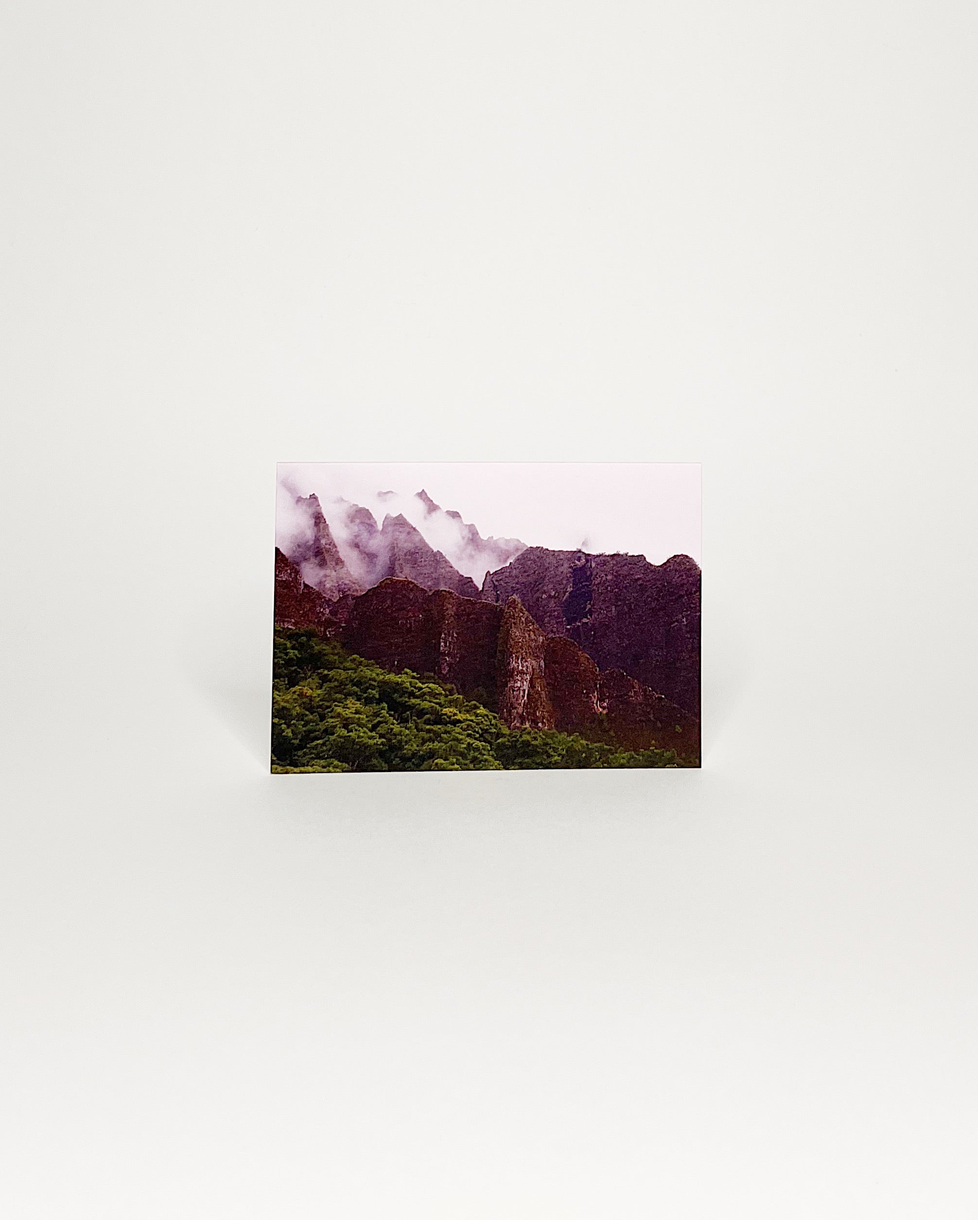 Photographic greeting card showcasing the mist-covered peaks of the Nā Pali Coast on Kauaʻi, with lush green forest in the foreground and dramatic ridgelines rising into the clouds
