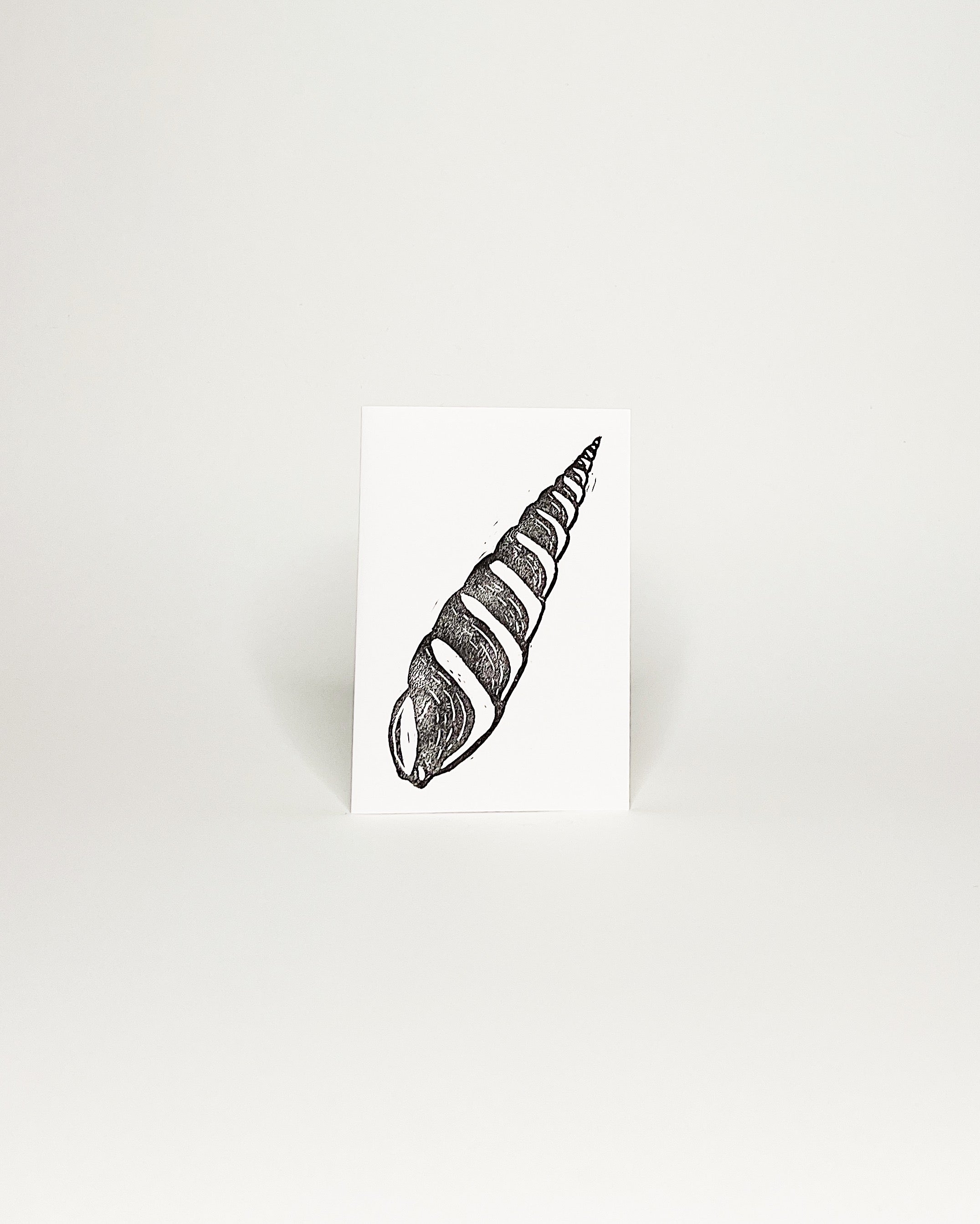 Minimalist black-and-white card featuring a hand made block print of a Hawaii spiral cone shell. White background.