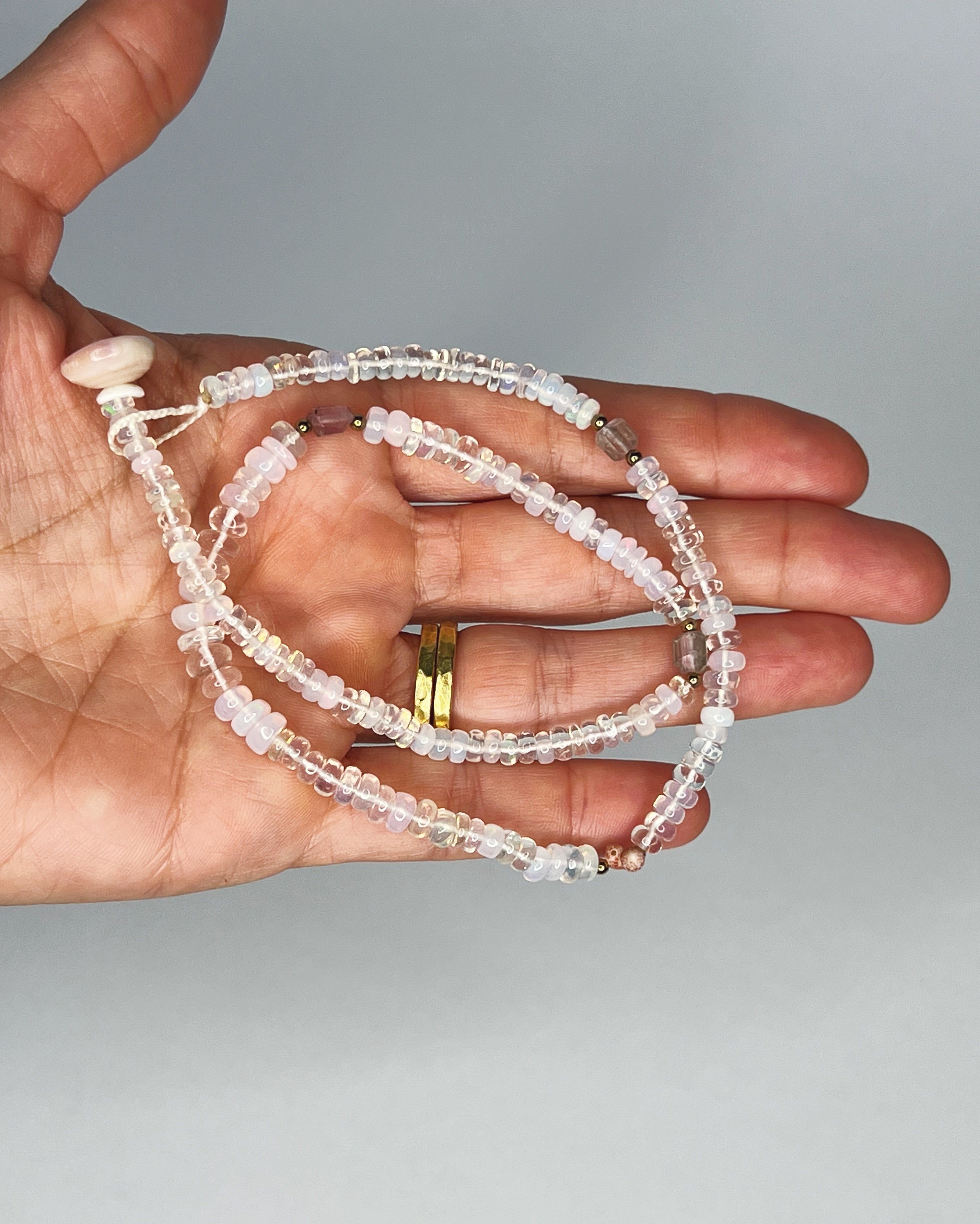 Hand holding Handmade opal choker with colorful tourmaline accents, puka shell clasp, white background