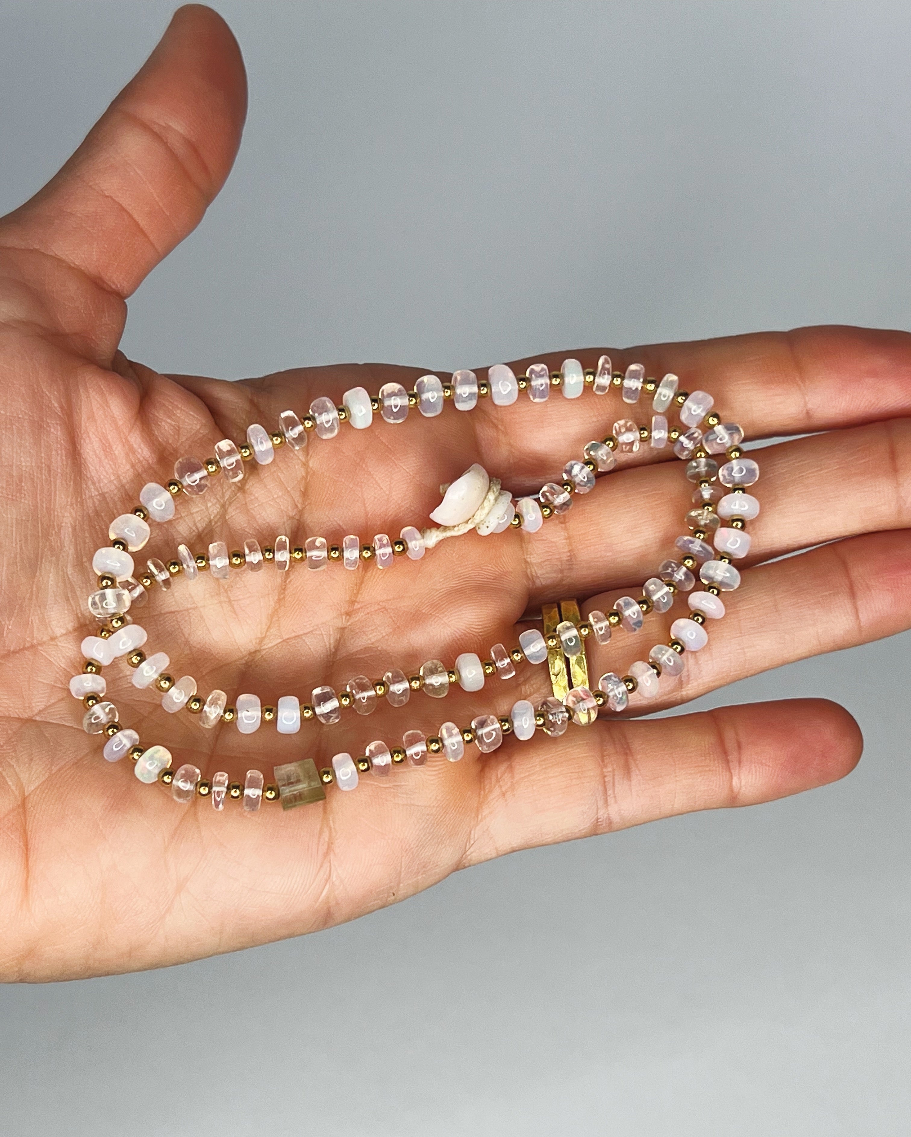 Hand holding Handmade opal choker with colorful tourmaline accent, gold spacer beads, puka shell clasp, white background