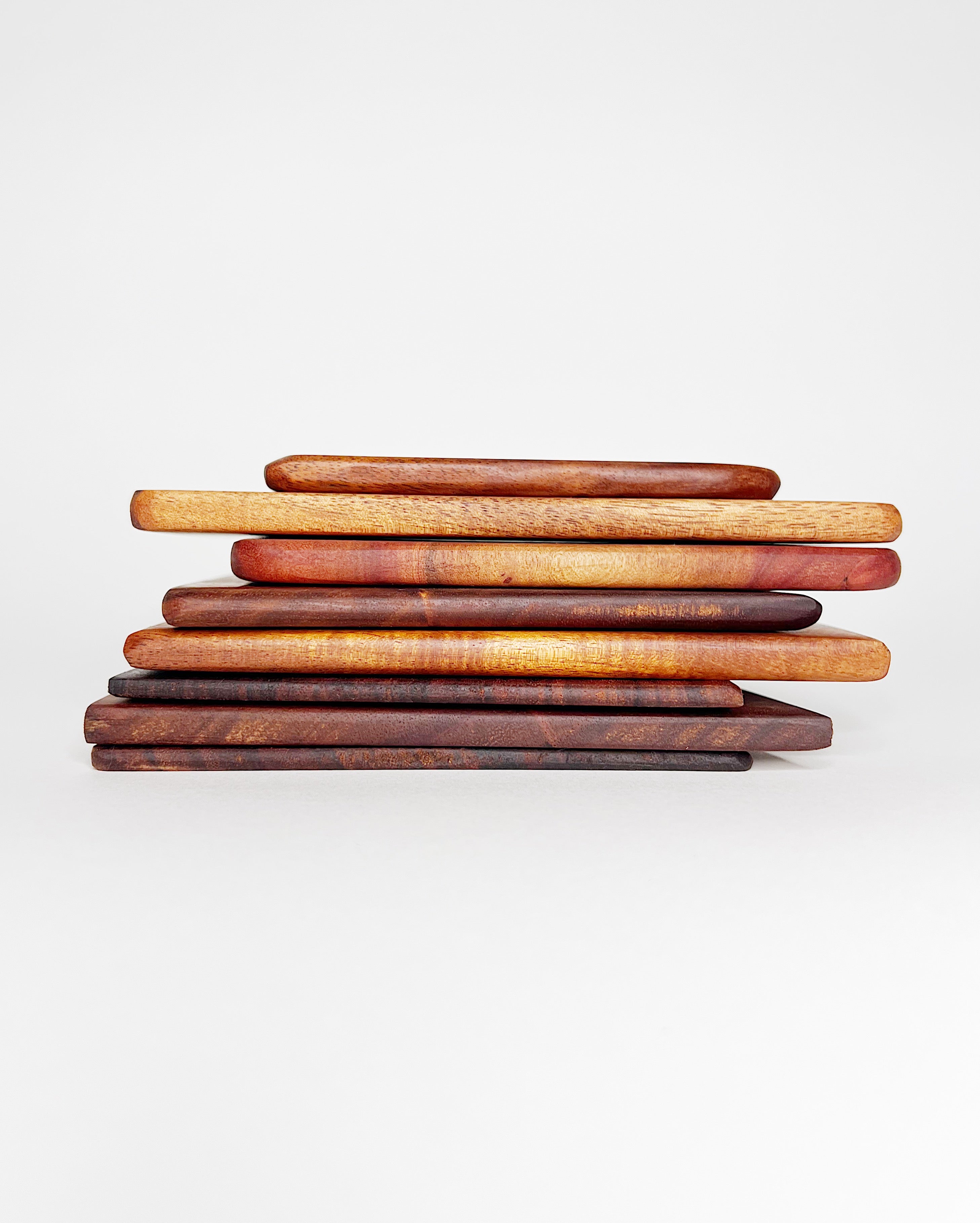 Stack of handmade Hawaiian hardwood cutting boards in varying shades of rich brown, red, and gold tones, displayed against a white background