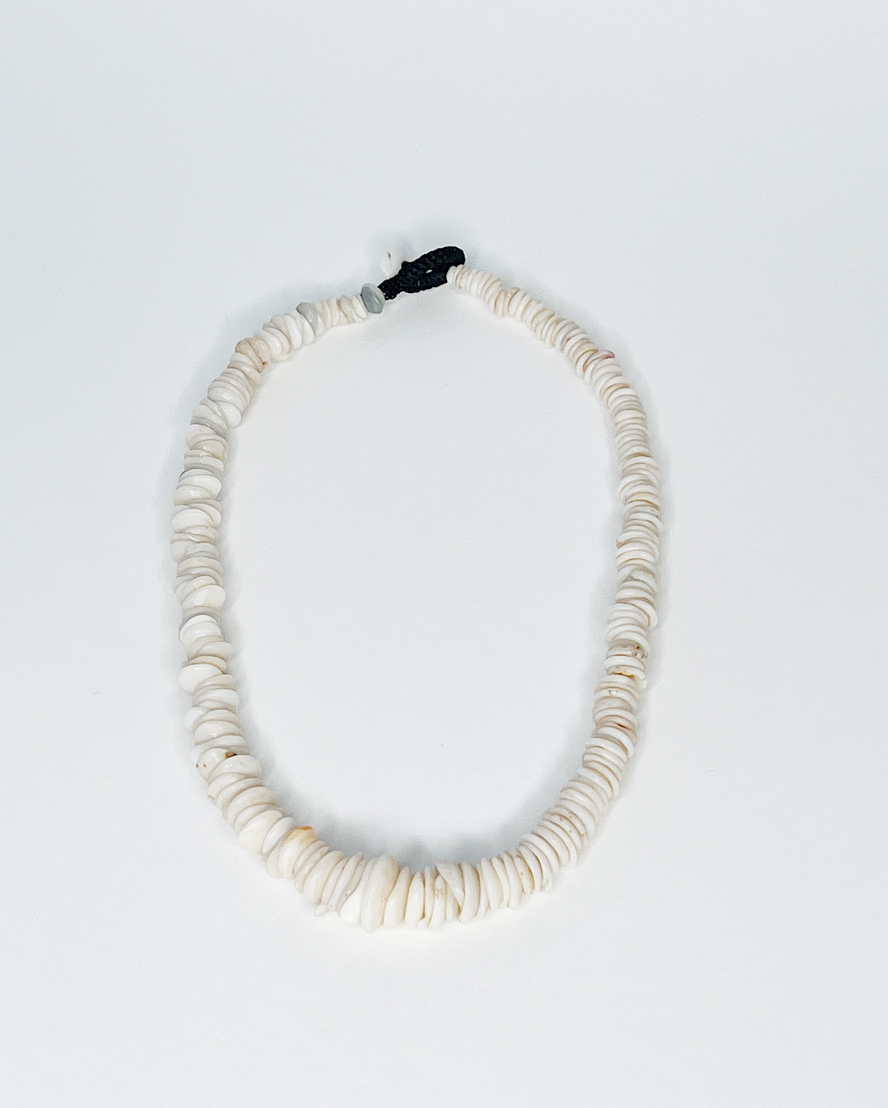 Expertly handcrafted puka shell necklace featuring naturally polished white and tan kauai puka shells strung on a durable black cord with a puka shell button clasp, displayed against a white background
