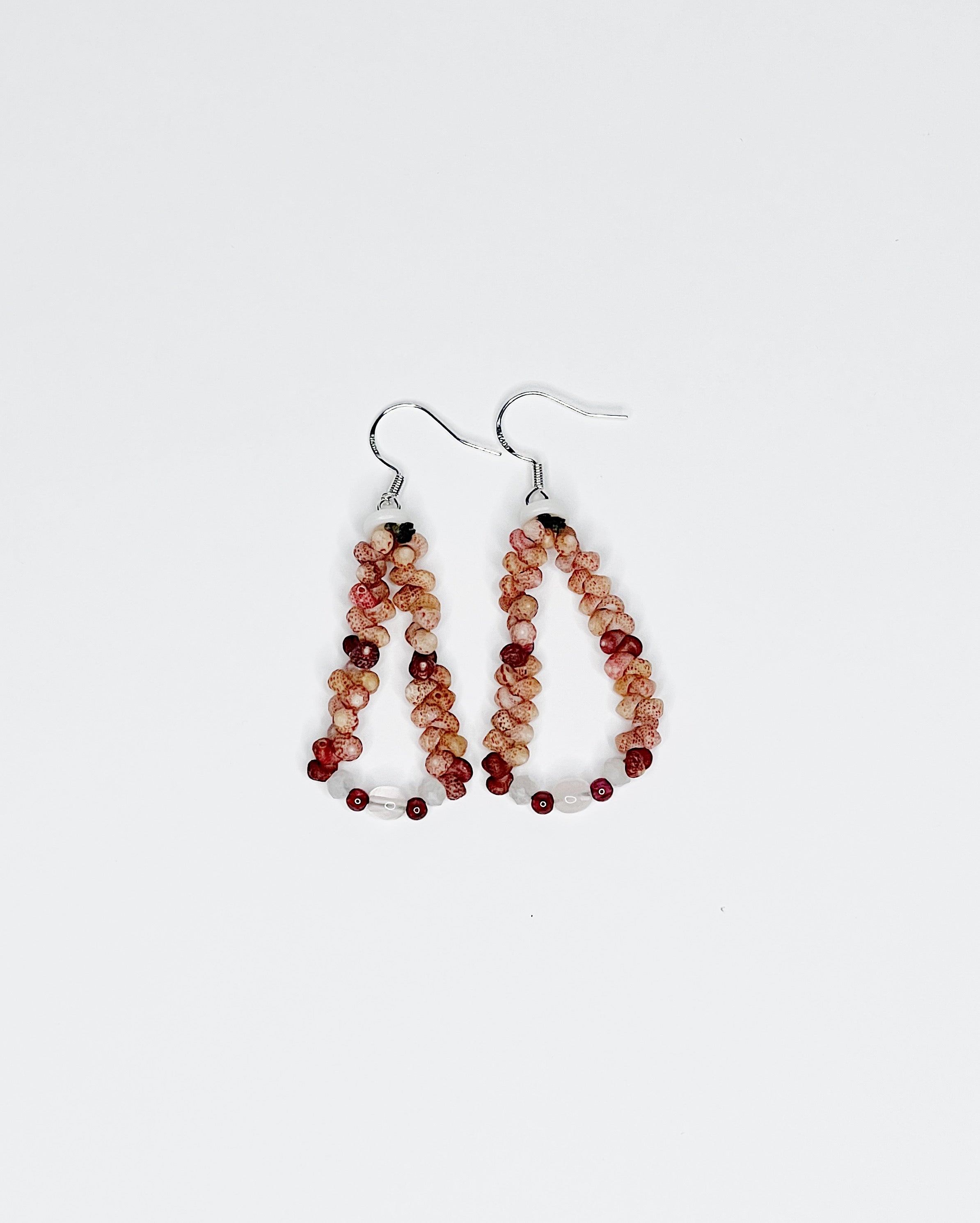 Handmade earrings featuring pink and red Kahelelani shells woven into a teardrop shape, accented with small moonstone beads at the base and finished with sterling silver hooks.