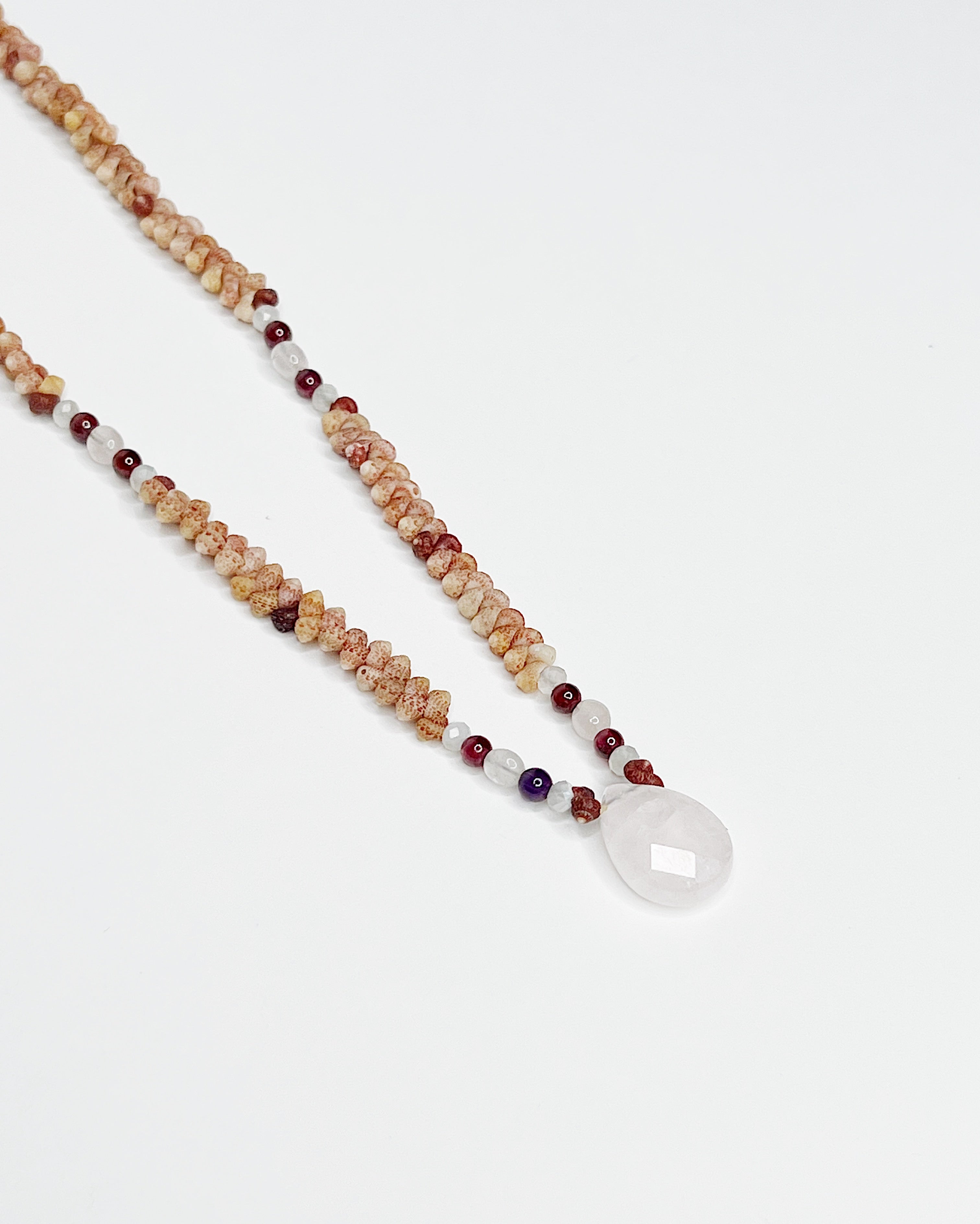 Handmade necklace featuring natural Kauaʻi Kahelelani shells intricately woven together, accented with garnet and moonstone beads and a faceted rose quartz teardrop pendant at the center, displayed against a white background