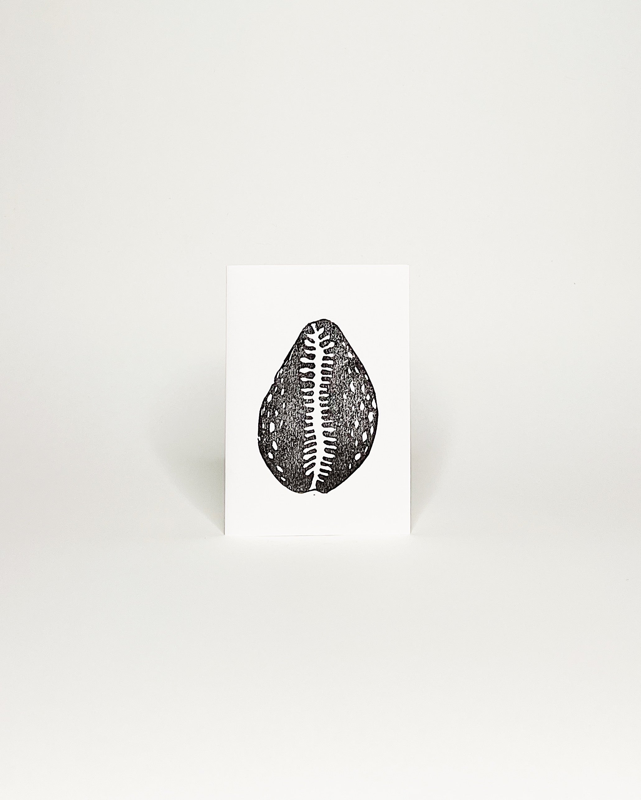 Minimalist black-and-white card featuring a hand made block print of a Hawaii cowrie shell. White background. 