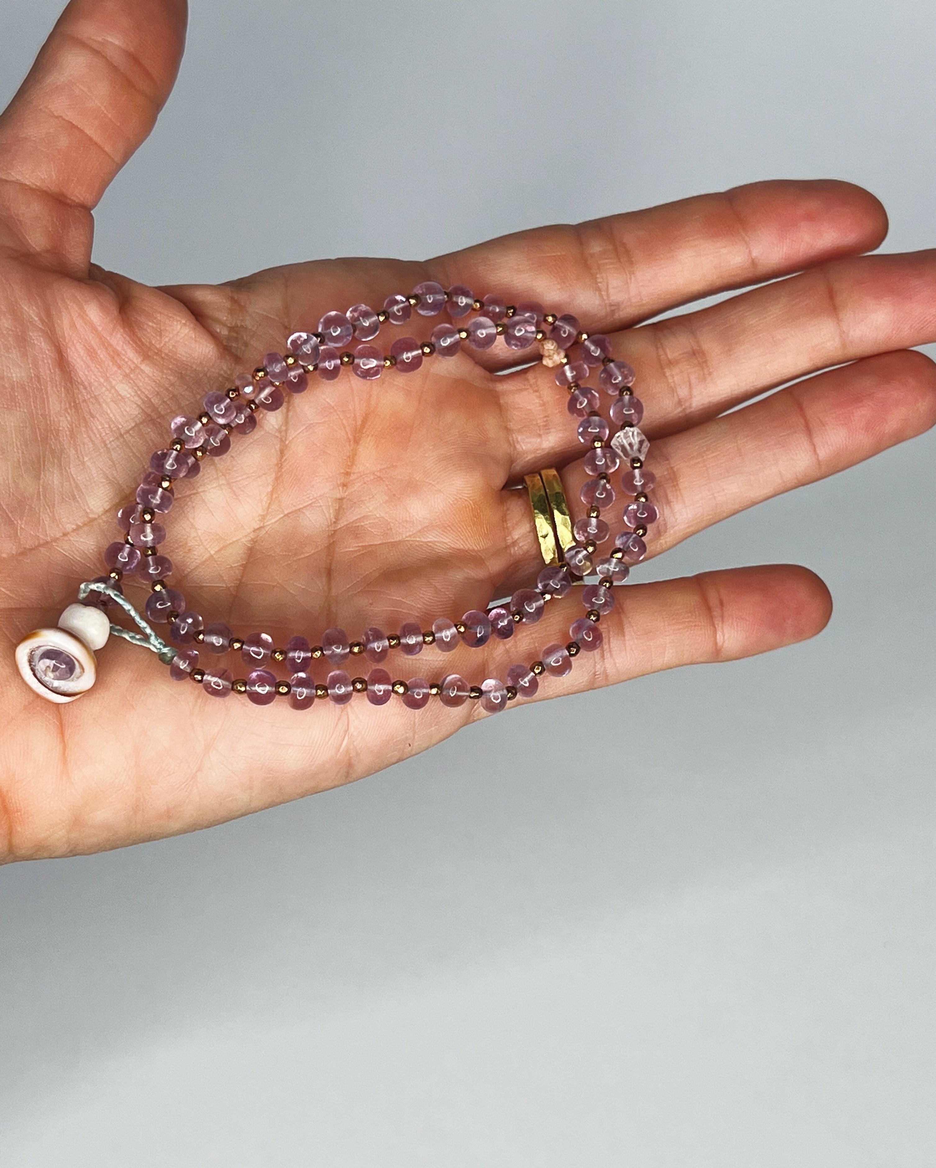 Hand holding Handmade amethyst choker with gold spacers, Kahelelani shell and tourmaline accents, finished with puka shell clasp. White background 