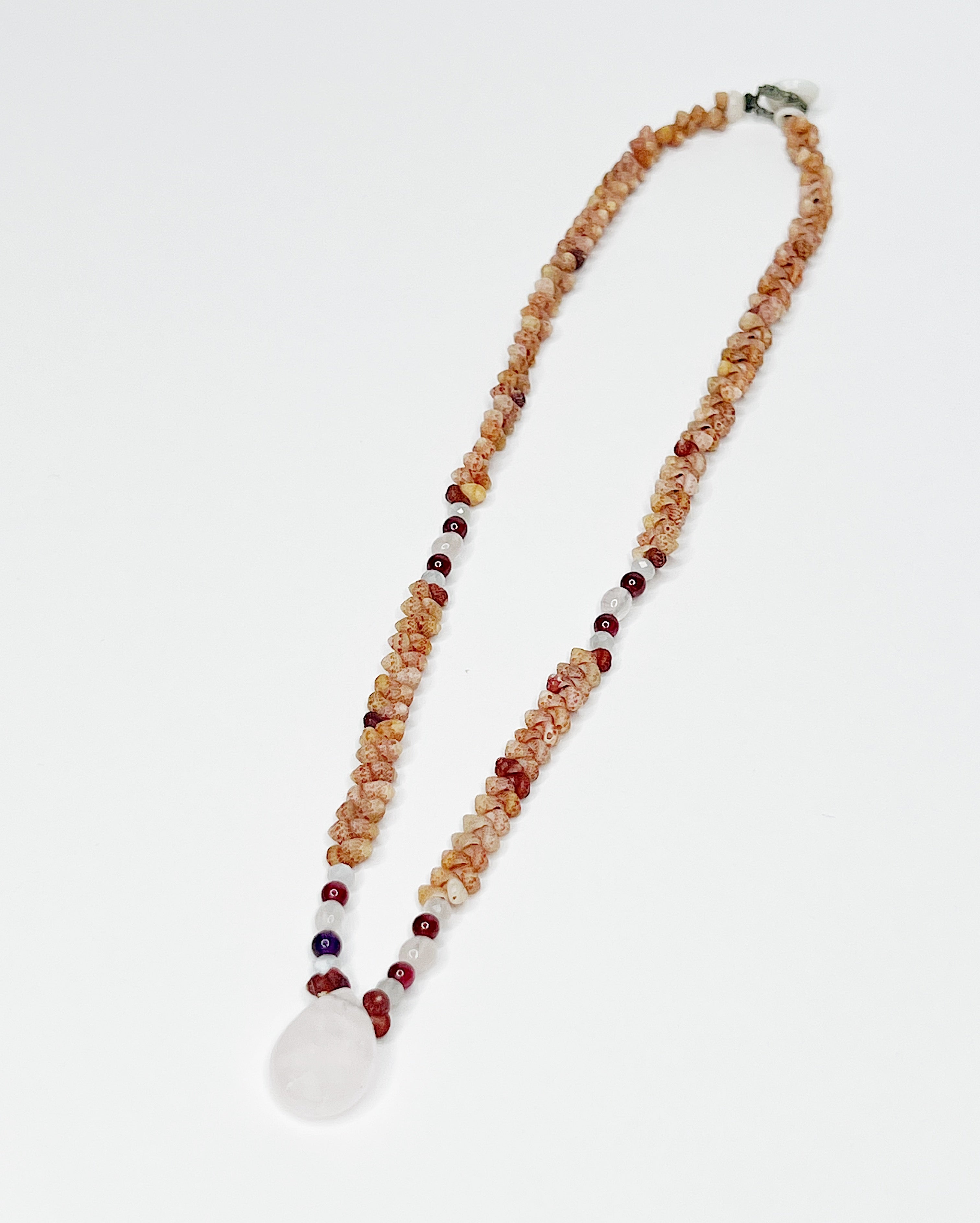 Handmade necklace featuring natural Kauaʻi Kahelelani shells intricately woven together, accented with garnet and moonstone beads and a faceted rose quartz teardrop pendant at the center, displayed against a white background