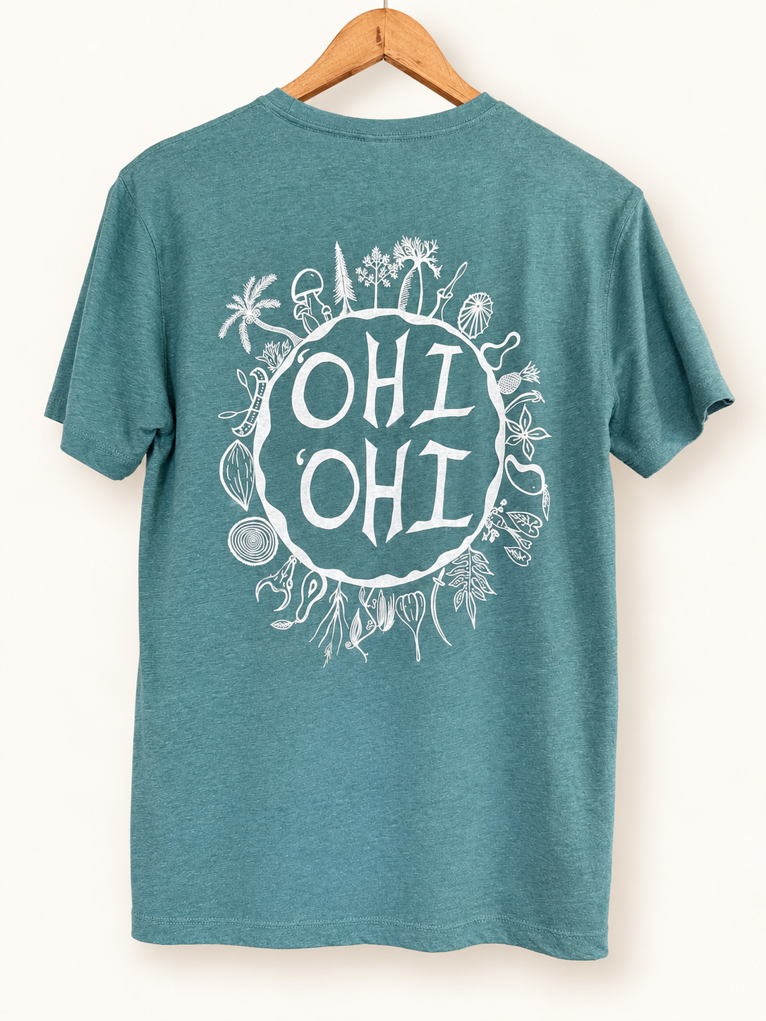 A teal heather short-sleeve t-shirt hanging on a wooden hanger against a warm off-white background. The back of the shirt features a large white circular graphic with the text 'OHI OHI' surrounded by hand-drawn tropical and nautical illustrations.